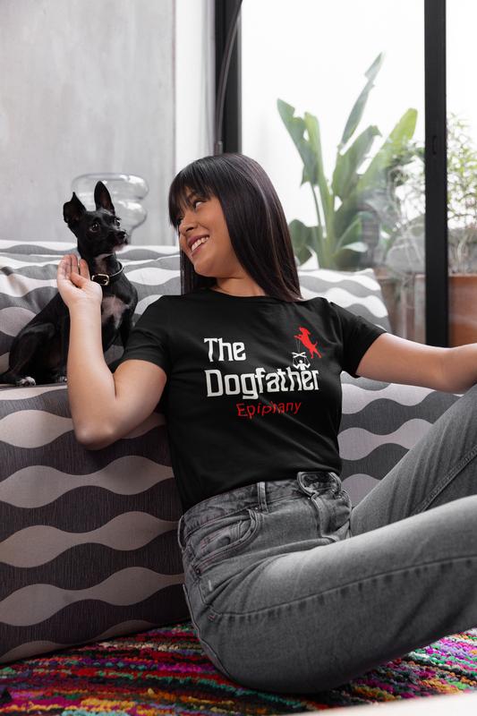 A young woman petting her little dog in her living room wearing a black t-shirt  featuring a playful twist on the classic “Godfather” design, with “The Dogfather” text and an image of a dog holding marionette strings, controlling its loyal human.  For all the dog lovers who know who's really in charge!